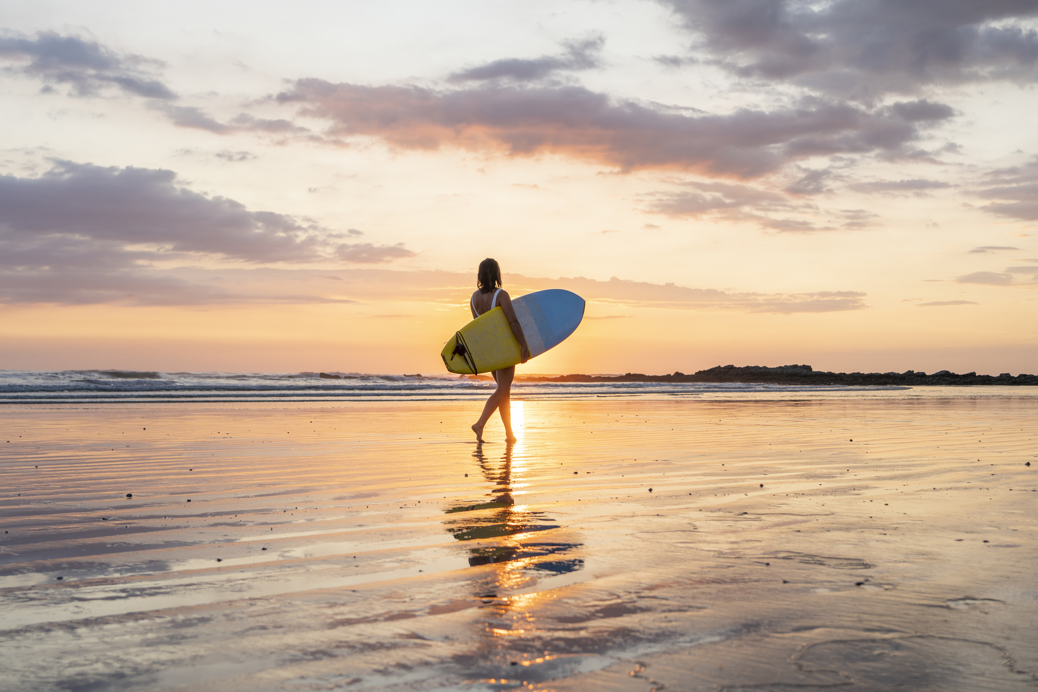 Surfer girl silhouette on the beach at sunset