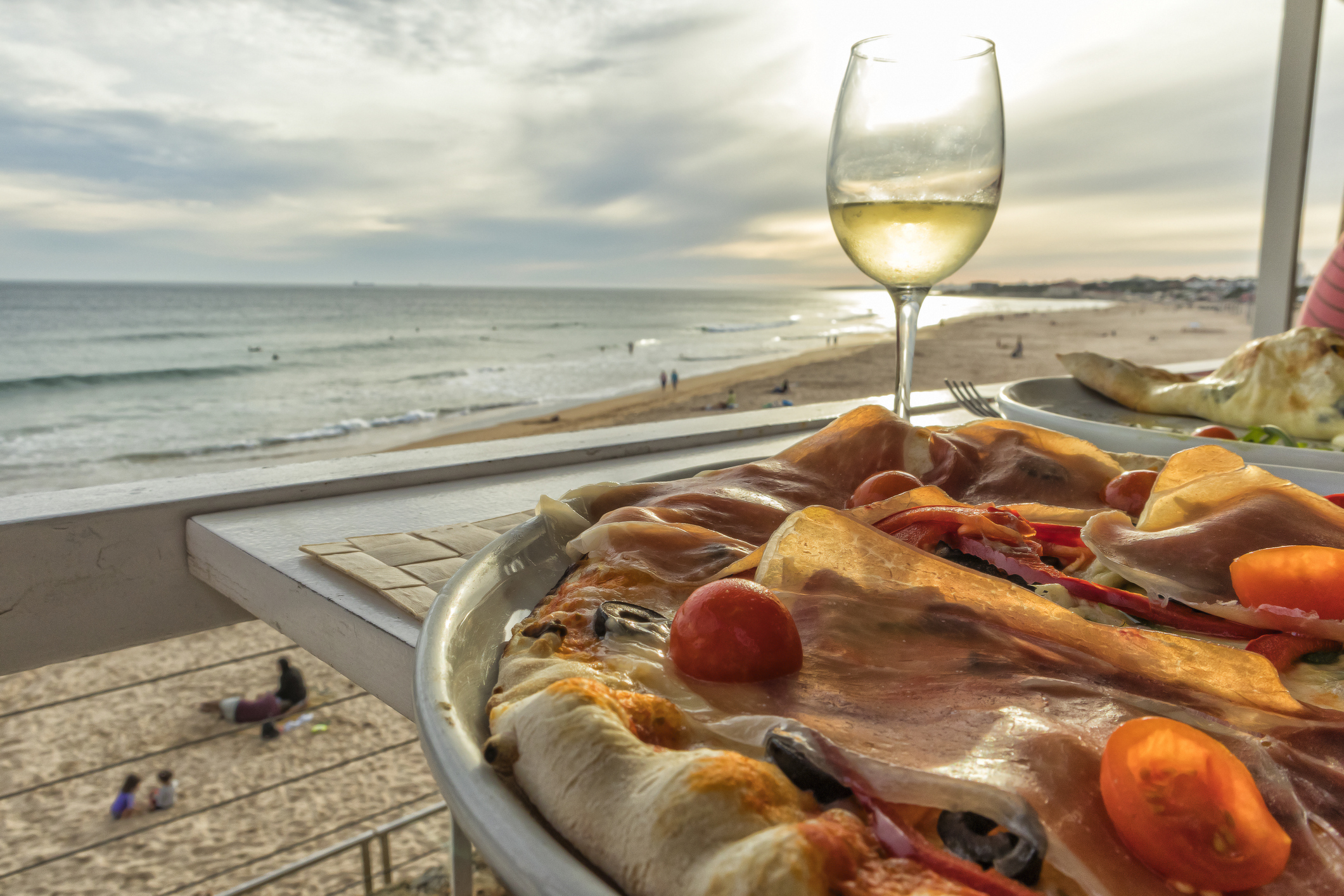 Homemade pizza with ham tomato olives and peppers with glass of white wine